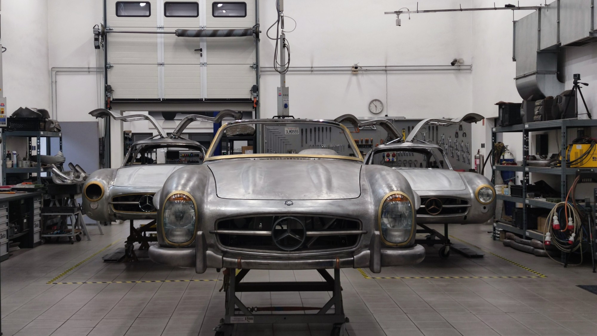 Three bare-metal 300 SL bodies in the workshop, a roadster in the middle and two Gullwing coupés with open doors