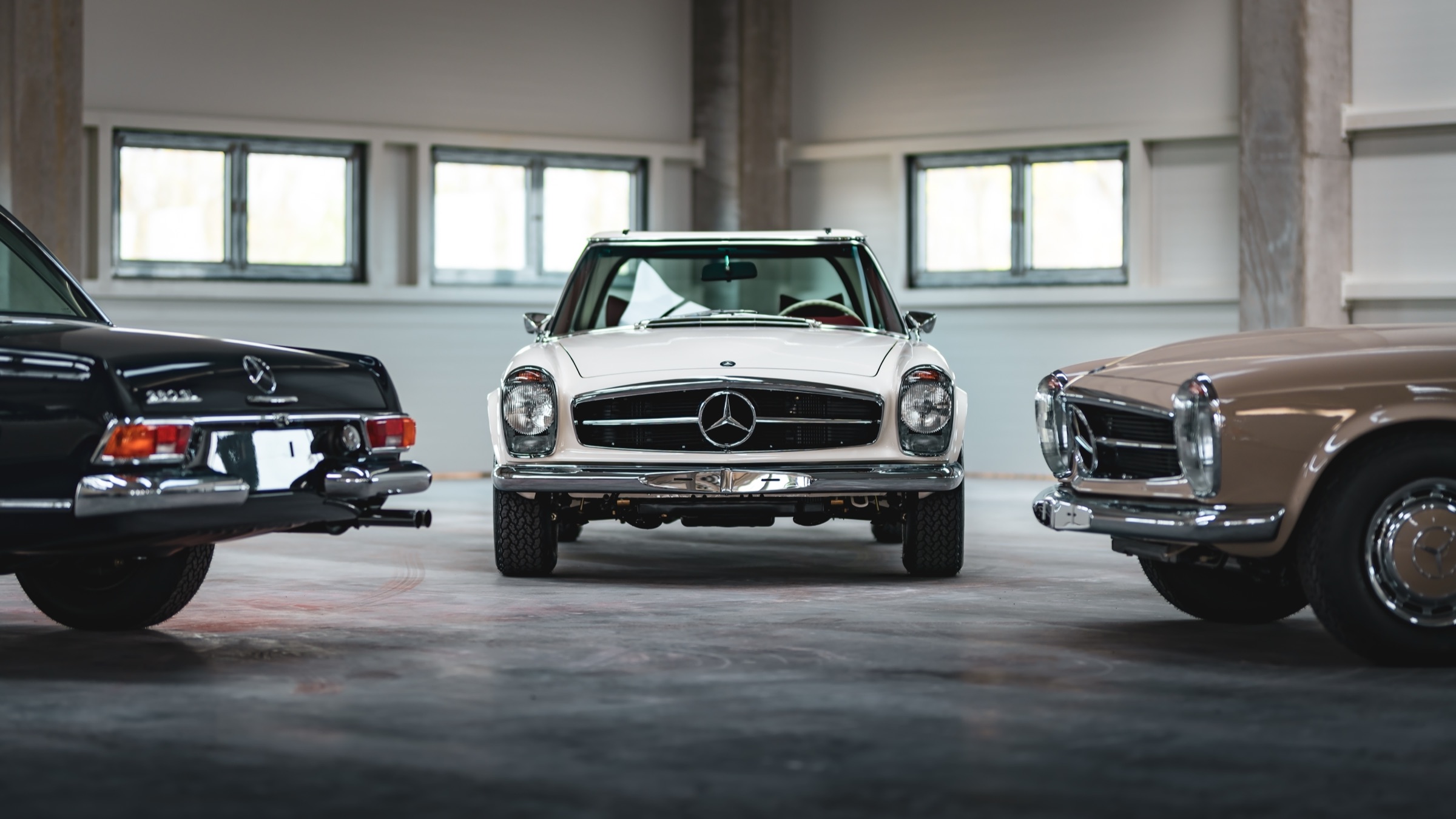 Cream Mercedes-Benz Pagoda seen from the front in the hall, between a black and a beige car