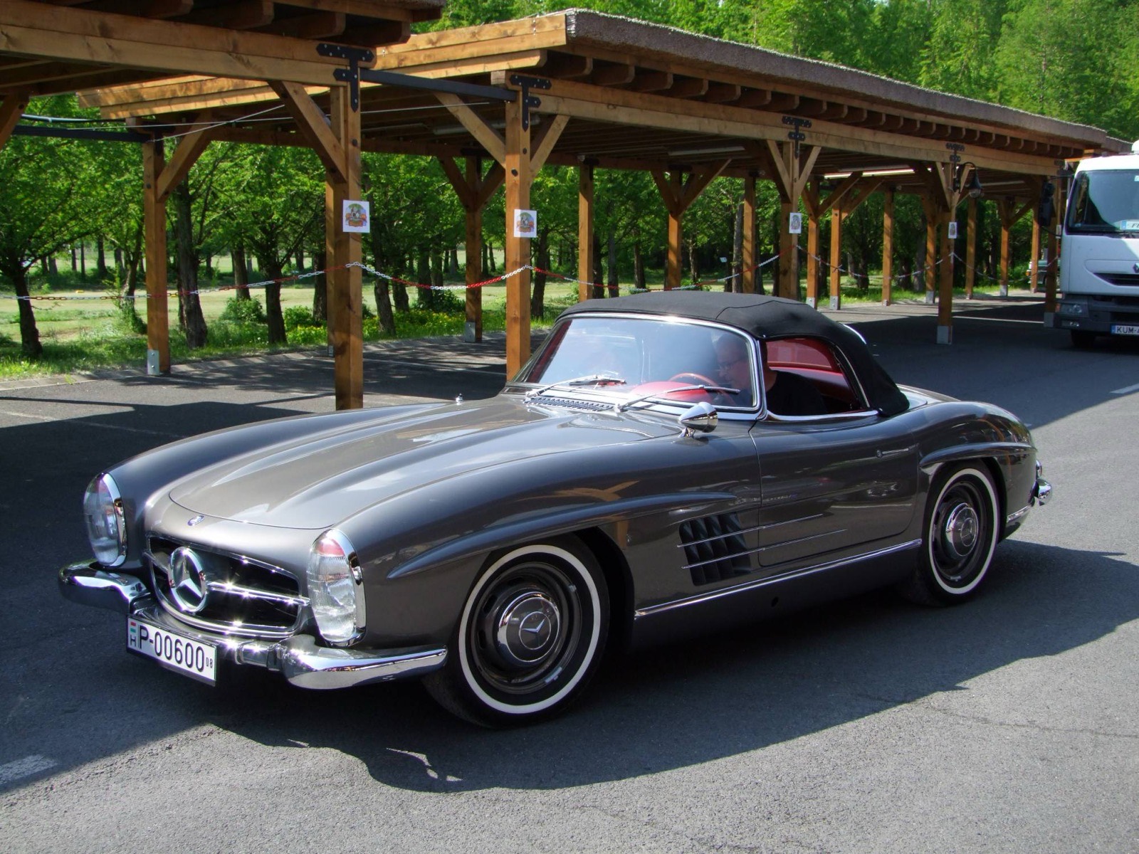 The grey Mercedes-Benz 300 SL Roadster with its black soft top, parked under the timber shelters at Hévíz