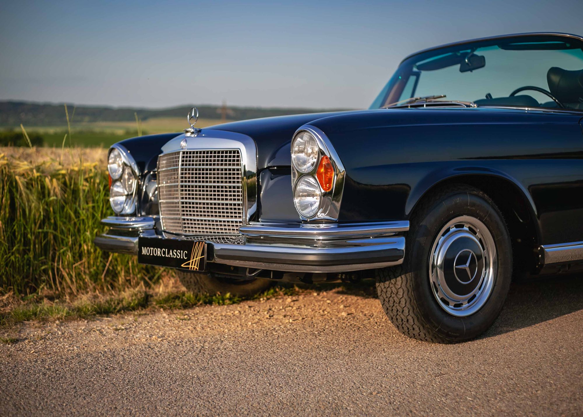 Front of a dark blue W111 convertible with chrome bumpers, twin headlamps and the Motor Classic plate