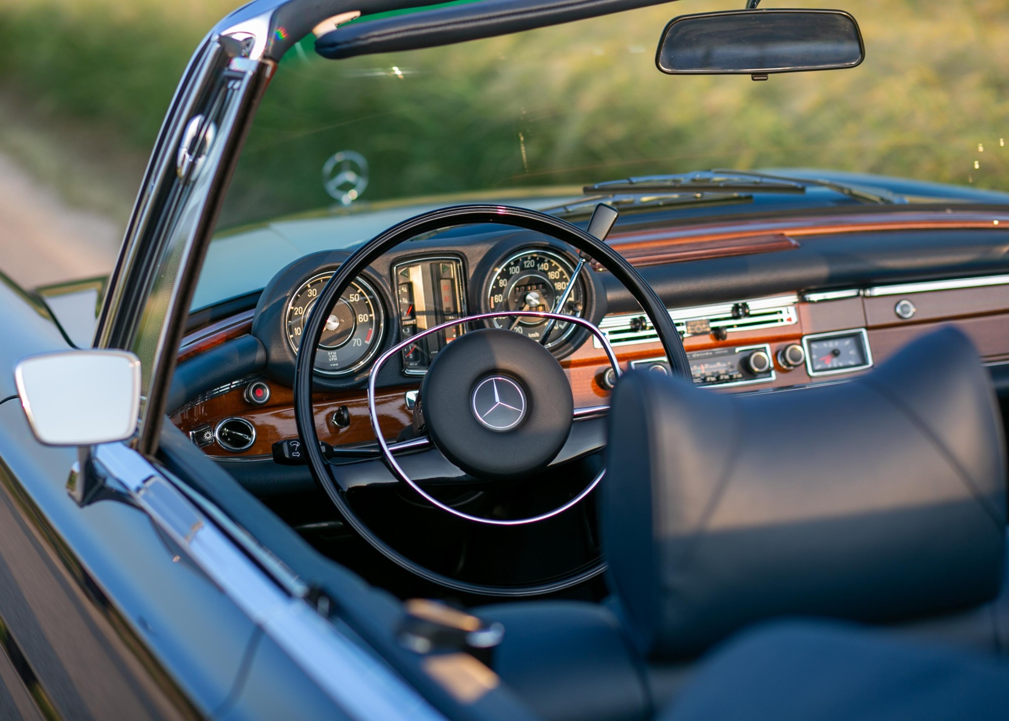 Steering wheel and wooden dashboard of a W111 convertible, seen from the driver's door with the road ahead